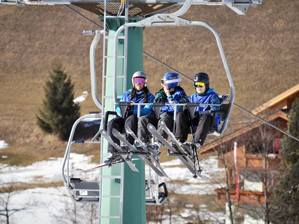 Drei Jugendliche fahren im Sessellift über das Tal.
